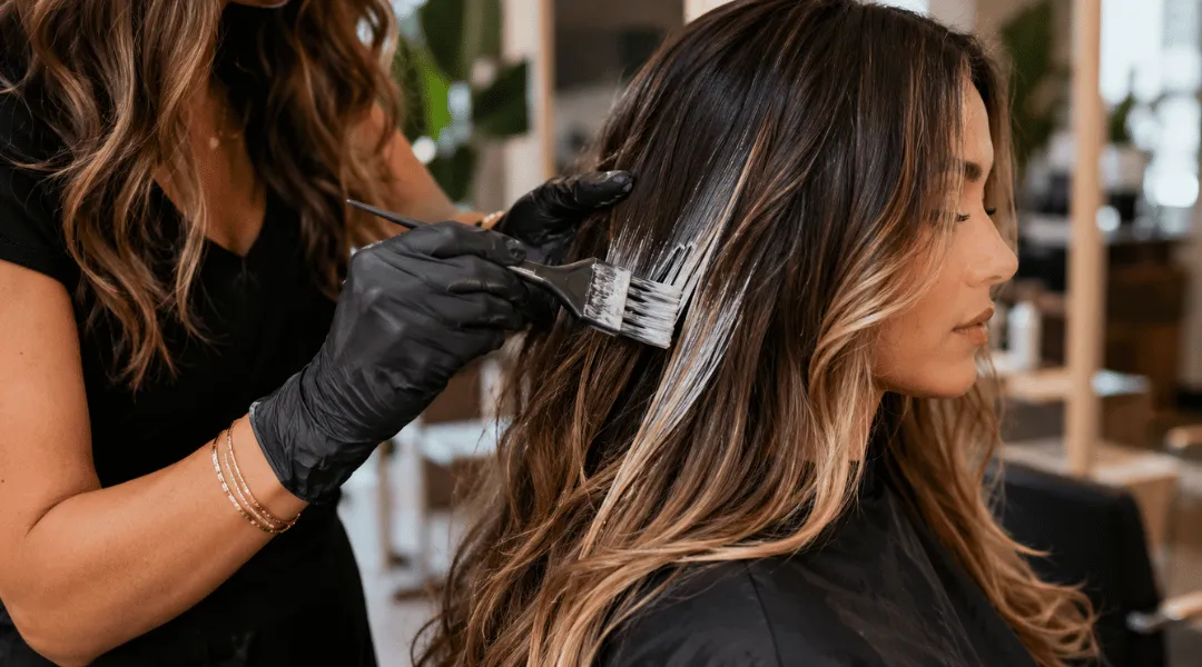 Professional hair colorist applying balayage highlights to a woman's hair